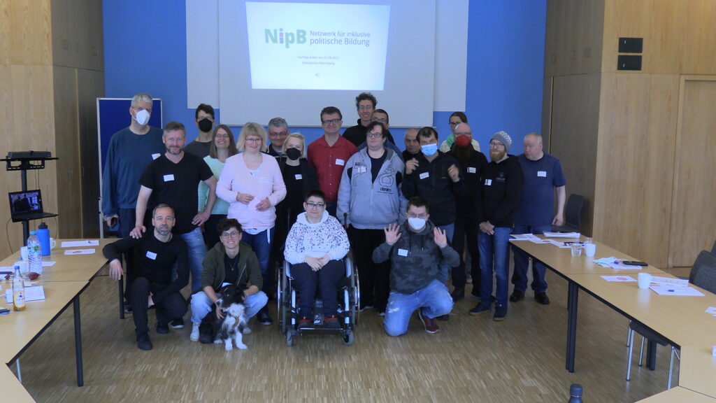 Gruppenfoto des NipB, mehrere Personen in 3 Reihen vor der Leinwand mit dem Logo des NipB