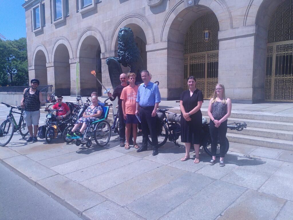 eine Gruppe Menschen steht vor einem Gebäude und einer Löwen-Statue, eine Person in der Mitte hält eine brennende Fackel