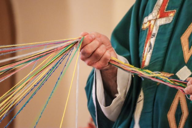 Hand des Dompfarrer hält viele bunte Fäden zusammen