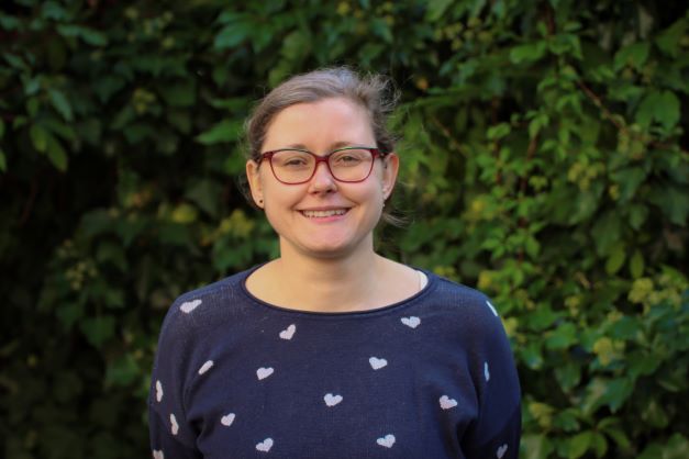 Brünette Frau in blauem Pullover vor grüner Hecke