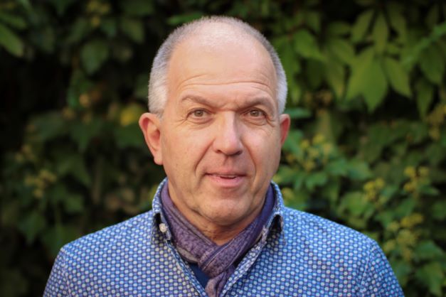 Porträtaufnahme Matthias Berke, er trägt ein blaues Hemd und steht vor einer Hecke