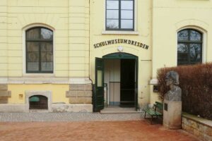 Eingang des Schulmuseums, grüne Flügeltür darüber der Schriftzug Schulmuseum Dresden, hellgelbes Gebäude