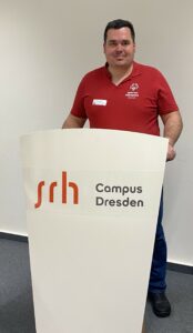 Andreas Sperling im roten Polshirt mit weißem Special Olympics Logo an einem Sprecherpult