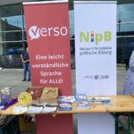 Zwei Rollups stehen hinter einem Stand, ein rotes mit dem Logo von Verso und ein weißes mit dem Logo des Netzwerks für inklusive politische Bildung