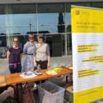 Juliane Heidelberger von Verso, Annika Gränz von der Volkshochschule und die Behindertenbeauftragte Manuela Scharf stehen hinter einem Stand
