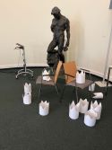 Weiße Papierkronen liegen vor einer schwarzen Skulptur auf dem Boden
