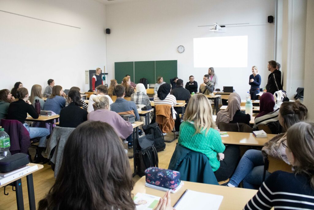 Schulklasse von hinten aufgenommen, im Tafelraum stehen die Teilnehmenden des Projekts TTT