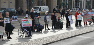 Menschen mit und ohne Behinderung in einer Reihe vor der Altmarktgalerie halten Plakate hoch