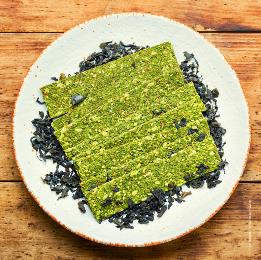 Weißer Teller mit grünen Spirulian-Crackern auf einem Holztisch