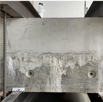 zwischen Stahlträger gespannte graue Betonwand, im unteren Bereich zerfressen und mit 2 Bohrungen versehen