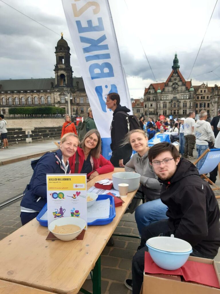 4 Personen an einem Biertisch, dahinter eine Flagge von Bike24 und im Hintergrund Brühlsche Terrasse und Residenzschloss