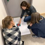 Drei Personen hockend um ein Flipchart auf dem Boden