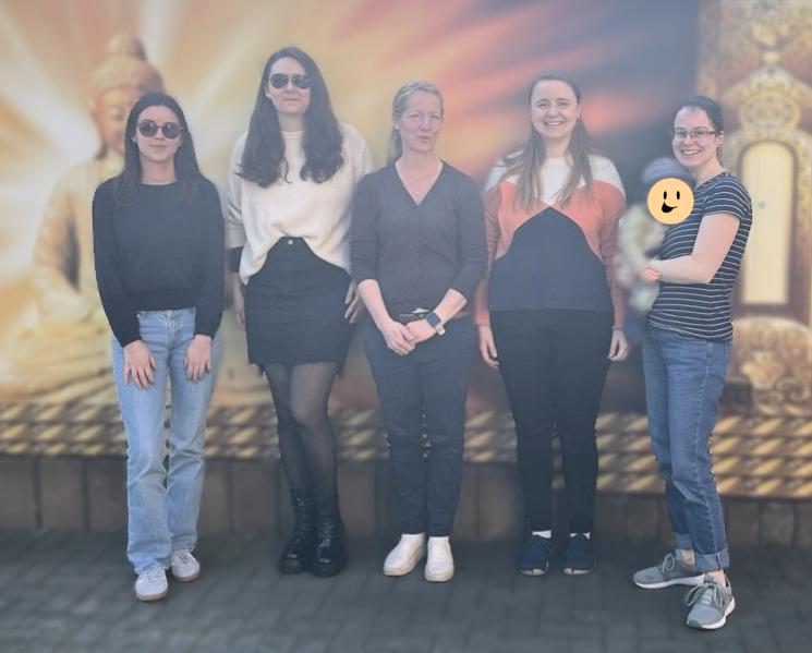 5 weiblich gelesene Personen stehen vor einer Fotowand und lächeln in die Kamera
