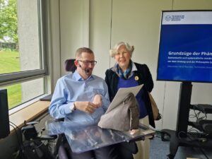 René und Professorin Gerl-Falkovitz in einem Seminarraum vor Fenster und Bildschirm