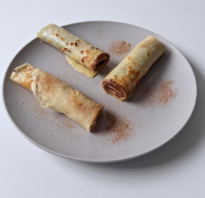 3 Eierkuchen mit Nutella zusammengerollt auf einem hellen Teller